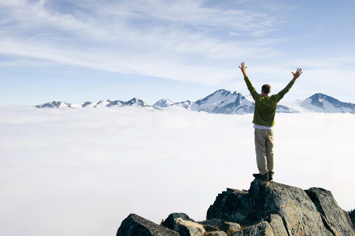 Personne levant les bras au ciel après avoir gravit une montagne. Il a atteinds son objectif